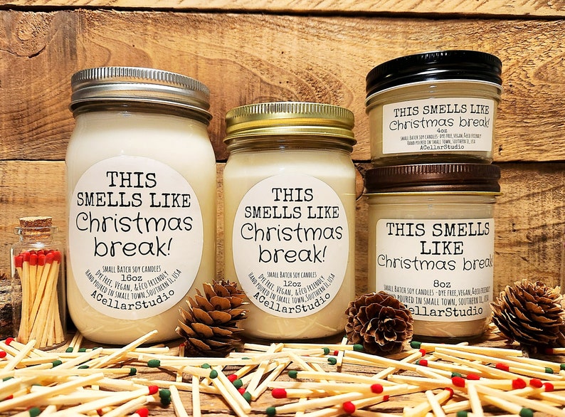 以下が含まれることがあります： ガラスの瓶に入ったソイワックスのキャンドル3本。ラベルには「This smells like Christmas break!」と書いてあります。キャンドルは1.6オンス、1.2オンス、8オンスの3つのサイズがあります。キャンドルは松ぼっくりとマッチが置かれた木製の表面の上に置かれています。