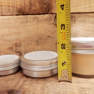 May include: Three different sized metal tins with lids. The largest tin is 2.5 inches tall and contains a light beige cream. The smaller tins are empty.