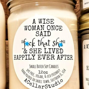 May include: A white jar candle with a black and blue label that reads "A wise woman once said "f*ck that sh*t" & she lived happily ever after." The label also includes the text "Small Batch Soy Candles", "12oz", "Dye Free, Vegan, & Eco Friendly", "Hand Poured in Small Town, Southern IL, USA", and "A Cellar Studio".