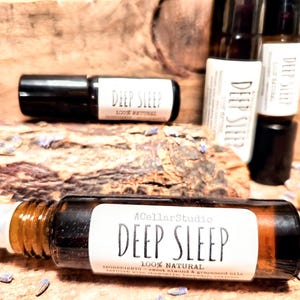 May include: A brown glass roller bottle with a white label that reads "A Cellar Studio Deep Sleep 100% Natural Ingredients: Sweet Almond &  Grapeseed Oil".