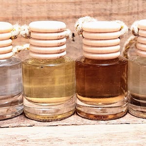 K&ouml;nnte beinhalten: Vier kleine Glasflaschen mit unterschiedlich farbigen Fl&uuml;ssigkeiten. Jede Flasche hat einen Holzdeckel und eine Schnur. Die Fl&uuml;ssigkeiten reichen von klar bis braun, was auf verschiedene D&uuml;fte oder &Ouml;le hindeutet.