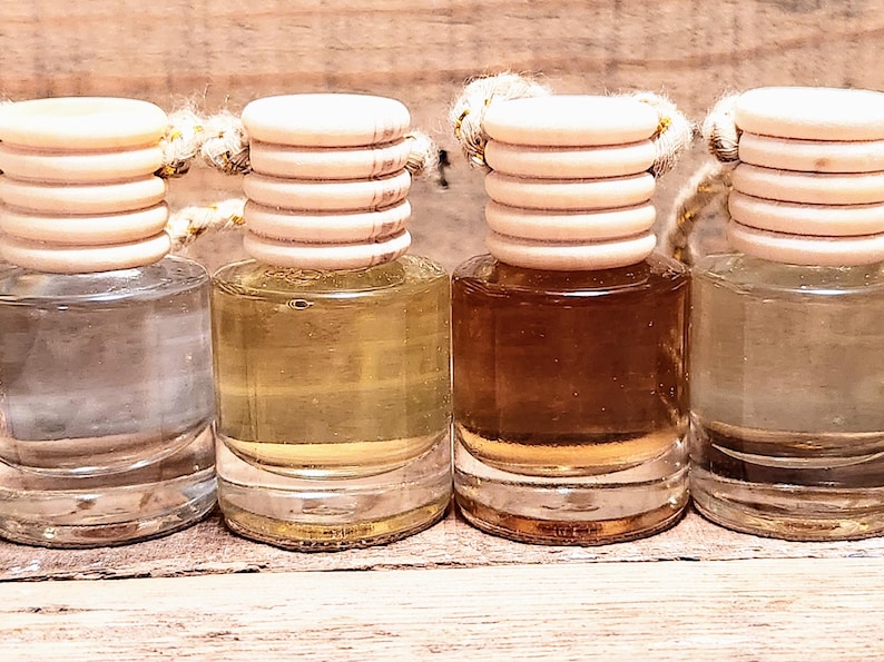 K&ouml;nnte beinhalten: Vier kleine Glasflaschen mit unterschiedlich farbigen Fl&uuml;ssigkeiten. Jede Flasche hat einen Holzdeckel und eine Schnur. Die Fl&uuml;ssigkeiten reichen von klar bis braun, was auf verschiedene D&uuml;fte oder &Ouml;le hindeutet.