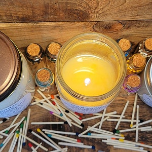 May include: Three glass jars with lids, two with white candles inside and one with a brown lid. The jars are surrounded by a scattering of wooden matches with colorful tips.