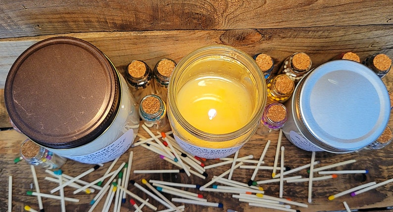 May include: Three glass jars with lids, two with white candles inside and one with a brown lid. The jars are surrounded by a scattering of wooden matches with colorful tips.