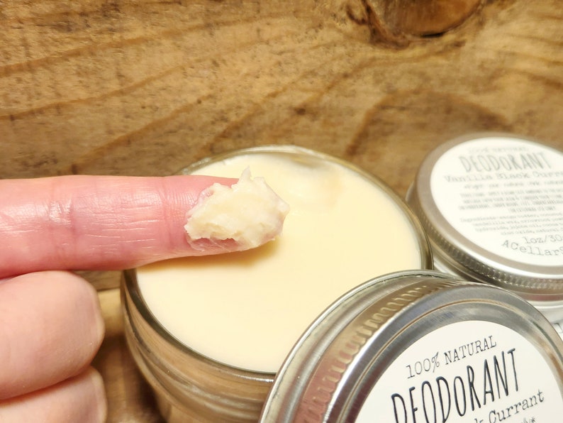 Puede incluir: Primer plano de un dedo que se introduce en un tarro de desodorante natural. El tarro est&aacute; etiquetado con "100% NATURAL DESODORANTE Grosella Negra".