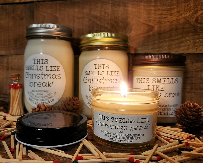 以下が含まれることがあります： ソイワックスキャンドルが入ったガラス瓶が3つ。瓶には「This smells like Christmas break!」とラベルが貼られており、木製のマッチで囲まれています。キャンドルはサイズが異なり、一番大きい瓶は160g、一番小さい瓶は4ozです。