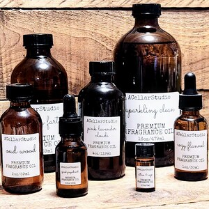 May include: A collection of amber glass bottles with labels for different premium fragrance oils. The labels include names like "oud wood", "pink lavender clouds", "sparkling clean", and "cozy flannel". The bottles are various sizes, ranging from 2 ounces to 16 ounces.