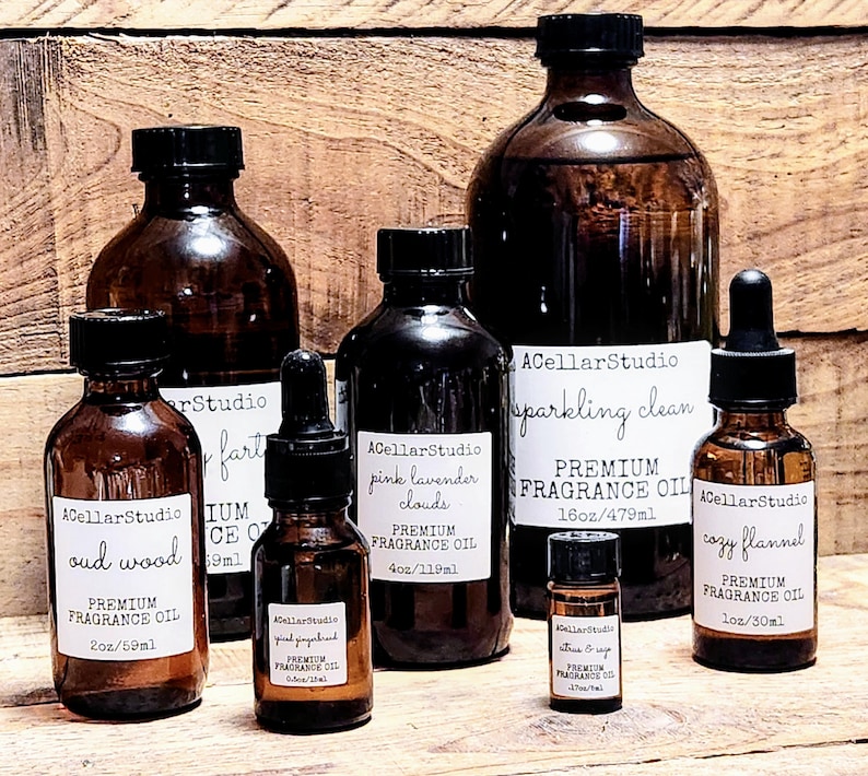 May include: A collection of amber glass bottles with labels for different premium fragrance oils. The labels include names like "oud wood", "pink lavender clouds", "sparkling clean", and "cozy flannel". The bottles are various sizes, ranging from 2 ounces to 16 ounces.