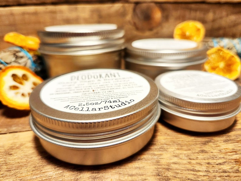 May include: Four silver metal containers with lids. The container in the foreground has a white label that reads "DEODORANT" and "2.5oz/74ml" and "A Cellar Studio".