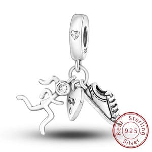 Könnte beinhalten: Ein silberner Charm-Anhänger mit einer rennenden Figur, einem Herz mit dem Wort "RUN" und einem Laufschuh. Der Charm besteht aus 925er Sterlingsilber und hat ein herzförmiges Design auf der Oberseite. Der Charm ist für ein Armband.