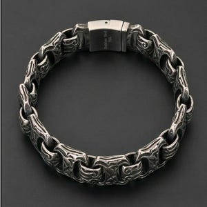 Puede incluir: Una pulsera de acero inoxidable plateado con un diseño ornamentado y texturizado. La pulsera presenta una serie de eslabones interconectados con patrones grabados. El cierre está marcado con el texto "Stainless Steel 316L".