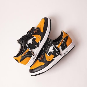 May include: A pair of black, white, and orange sneakers with a unique design. The shoes feature a white sole, orange accents, and a stylized graphic on the side. Text on the shoes reads "TIGER STYLE", "DA Ruckf", "TOAD STYLE", and "BRING".