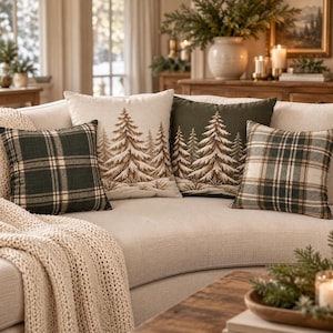 May include: Four square throw pillows arranged on a sofa. Two pillows feature a dark green and cream plaid pattern. The other two pillows are cream and dark green, each displaying an embroidered forest of pine trees in brown and white.