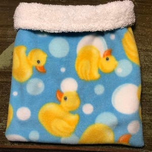 May include: A blue fleece pouch with a pattern of yellow rubber ducks and white bubbles. The top edge is trimmed with soft, white, fluffy material. The pouch is designed for small items.
