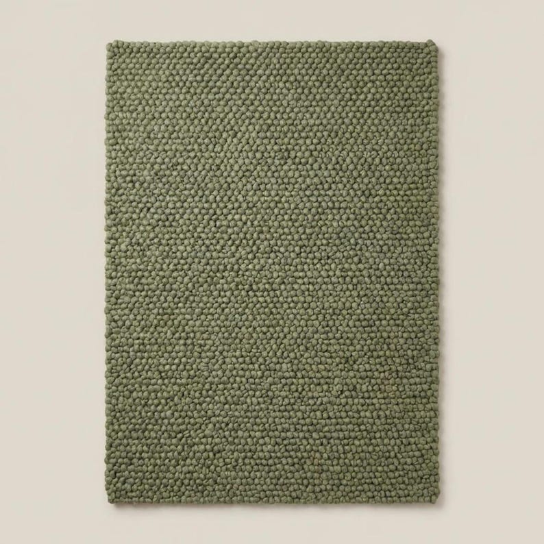 May include: A rectangular area rug in a solid olive green color. The surface of the rug features a dense, uniform texture composed of small, rounded, pebble-like tufts arranged in a consistent grid pattern across the entire rectangular piece.