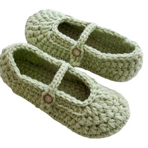 May include: A pair of light green crocheted slippers with a button detail. The slippers have a strap that goes over the foot.