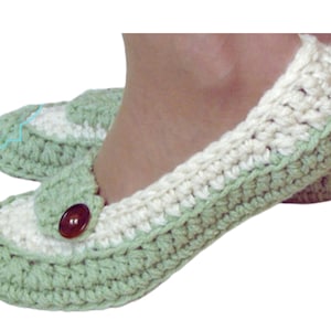 May include: A pair of green and white crocheted slippers with a button detail. The slippers are made with a soft yarn and have a comfortable fit.