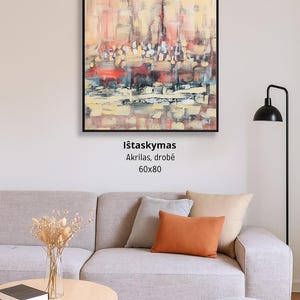 Könnte beinhalten: Abstraktes Acrylgemälde in einem schwarzen Rahmen, das eine Stadtlandschaft in Rot-, Gelb- und Blautönen zeigt. Das Kunstwerk ist 60x80 cm groß. Das Gemälde hängt über einem grauen Sofa mit orangefarbenen und neutralfarbenen Kissen.