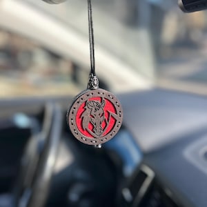 Peut inclure: Un diffuseur de parfum pour voiture en bois rond avec un motif de tête de cheval. Le cheval est marron sur fond rouge, encadré d'une bordure marron foncé. Il est suspendu à un cordon noir.