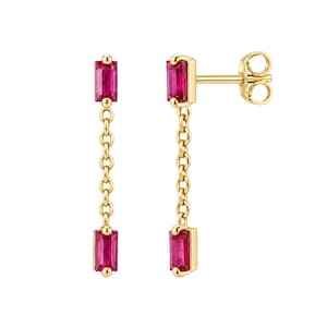 May include: A pair of gold drop earrings featuring two rectangular baguette-cut red rubies connected by a delicate gold chain. The top ruby serves as the stud post, while the second ruby hangs at the base of the chain, secured with a butterfly back.