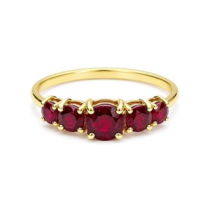 Puede incluir: Un anillo de oro con cinco piedras preciosas rojas redondas y vibrantes. Las piedras están engastadas en una fila en la parte superior del anillo, con una banda de oro pulido. El anillo se muestra sobre un fondo blanco.