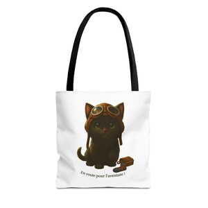 May include: White tote bag featuring a cartoon black cat wearing a brown aviator helmet and goggles. The cat is sitting next to a brown boot. The text "En route pour l'aventure!" is printed at the bottom.