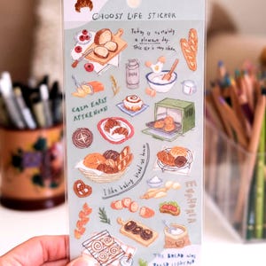 Puede incluir: Una lámina de pegatinas transparente con ilustraciones de panadería, incluyendo pan, pasteles y utensilios de cocina. El texto incluye "BAKE BREAD", "CHOOSY LIFE STICKER", y "THE BREAD WAS BAKED LIGHT AND FLUFFY".