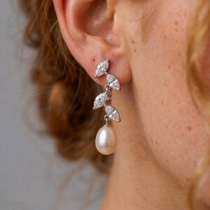 May include: Elegant drop earrings featuring three marquise-cut cubic zirconia stones and a lustrous pearl. The earrings are crafted in a silver-tone metal, creating a sophisticated and timeless design. Perfect for special occasions or everyday wear.