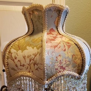 May include: A pair of ornate gold candle holders with crystal accents and a floral patterned lampshade with a beaded fringe.