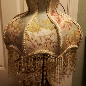 May include: A vintage table lamp with a floral patterned lampshade and a gold base. The lampshade has a beaded fringe and a scalloped edge.