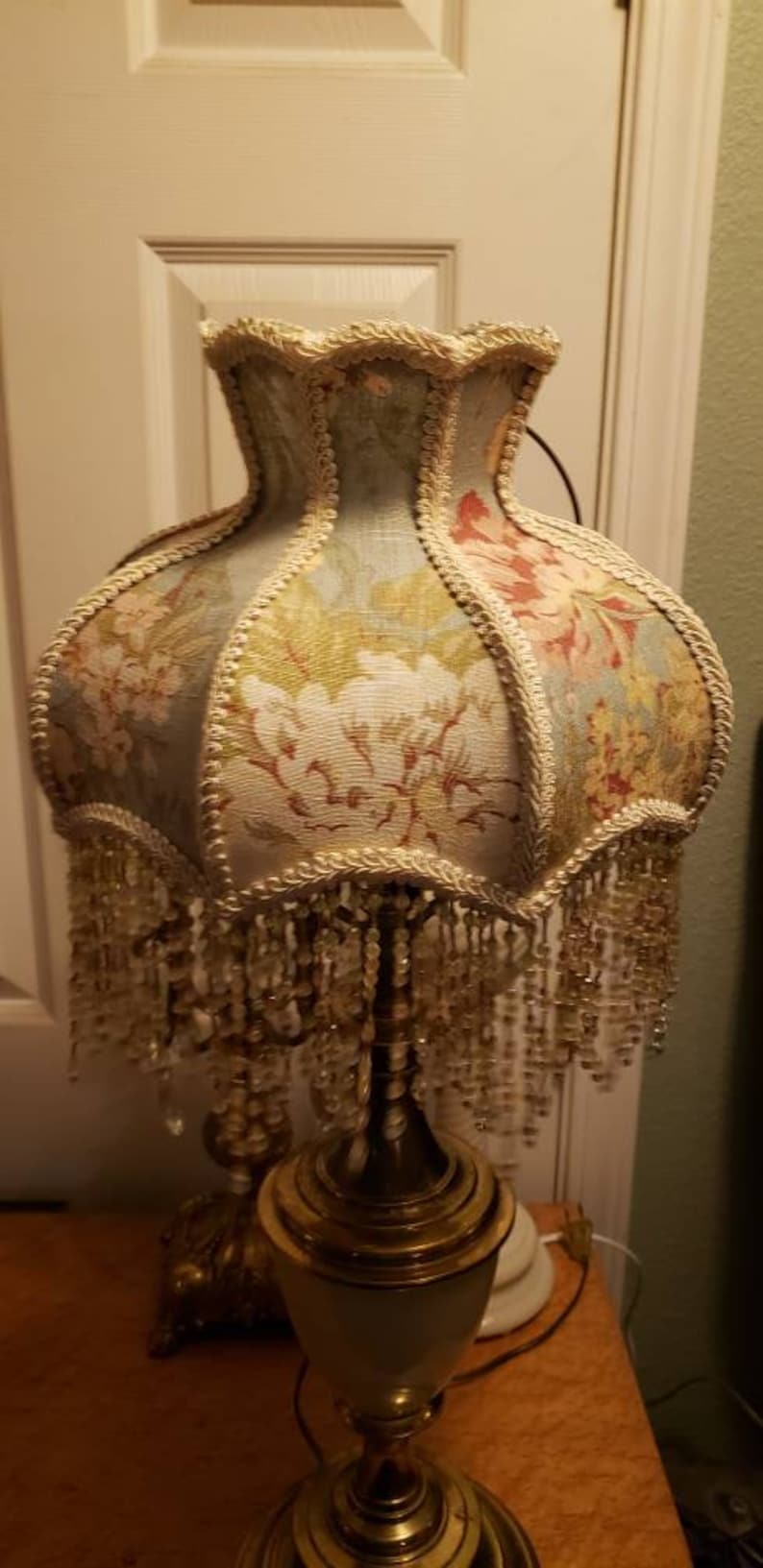 May include: A vintage table lamp with a floral patterned lampshade and a gold base. The lampshade has a beaded fringe and a scalloped edge.