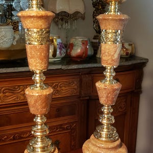 May include: Two vintage table lamps with a marble effect, peach-coloured body and gold-toned metal accents. The lamps have a classic design with ornate detailing. They are likely from the mid-century era and are placed on a wooden surface.