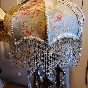 May include: A vintage lamp with a floral patterned lampshade and crystal bead fringe. The lamp base is gold metal with a decorative design and crystal accents.