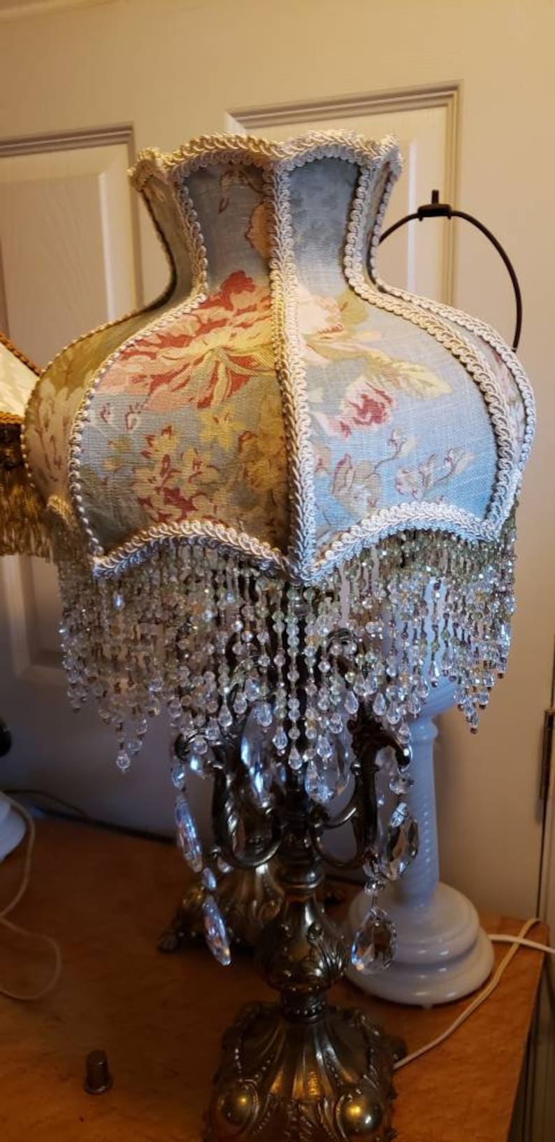 May include: A vintage lamp with a floral patterned lampshade and crystal bead fringe. The lamp base is gold metal with a decorative design and crystal accents.