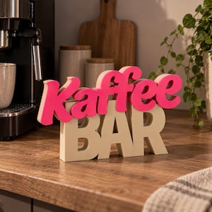 Könnte beinhalten: Ein freistehendes Dekoschild mit dem Wort Kaffee in leuchtend pinker Schreibschrift, das über dem Wort BAR in beigen Blockbuchstaben angebracht ist. Das Schild ist mehrschichtig aufgebaut und erzeugt so einen dreidimensionalen Effekt.