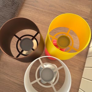 May include: Three colorful lampshades: a brown, a yellow, and a white one. The brown lampshade is cylindrical, the yellow one is a cone shape, and the white one is a cylinder. Each lampshade has a metal frame and a mesh screen at the bottom.