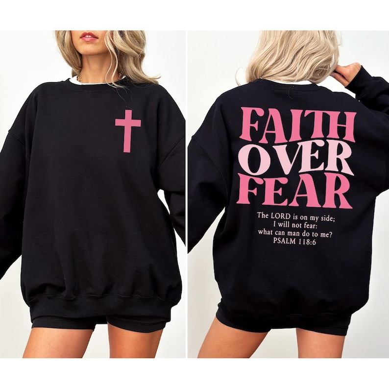 May include: Black sweatshirt with a pink cross on the front and "FAITH OVER FEAR" printed on the back. The back also includes the Bible verse Psalm 118:6. The sweatshirt has a white crew neck.
