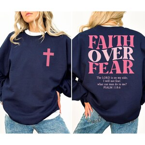 May include: Navy blue sweatshirt with a pink cross on the front and the words "FAITH OVER FEAR" on the back. The text "The LORD is on my side; I will not fear: what can man do to me? PSALM 118:6" is below the main text.