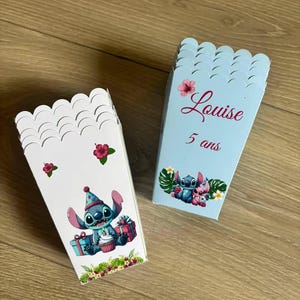 Peut inclure: Deux boîtes à popcorn bleues claires et blanches avec des bords festonnés. Une boîte présente un personnage de dessin animé avec un chapeau d'anniversaire et des cadeaux. L'autre boîte porte le nom "Louise" et "5 ans".