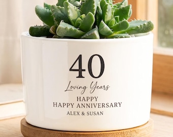 May include: A white ceramic cylindrical planter with a bamboo saucer containing a green succulent. The planter features black text that reads 40 Loving Years, HAPPY HAPPY ANNIVERSARY, and the names ALEX & SUSAN printed on the front surface.