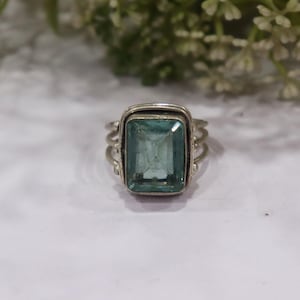 May include: A silver ring featuring a large, rectangular, light blue gemstone. The ring has a triple-band design on each side of the gemstone, adding a unique detail. The gemstone is set in a rectangular frame.