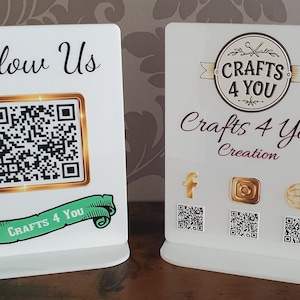 May include: Two white rectangular acrylic signs with stands. The left sign features the text Follow Us, a gold-bordered QR code, and a green banner reading Crafts 4 You. The right sign displays the Crafts 4 You logo, social media icons, and QR codes.
