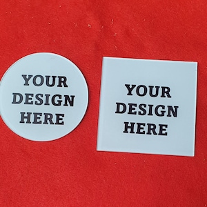 May include: Two custom coasters, one round and one square, with the text "YOUR DESIGN HERE" in black block letters. The coasters are white and sit on a red surface.