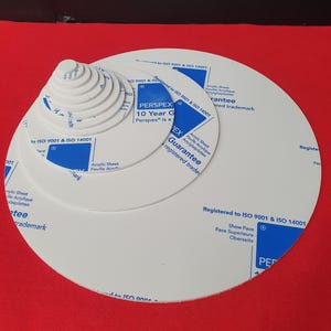 May include: A collection of white Perspex acrylic sheets in a spiral arrangement, with blue and white printed text. The sheets are of different sizes, with the largest at the bottom. Text includes "Guarantee" and "Registered to ISO 9001 & ISO 14001".