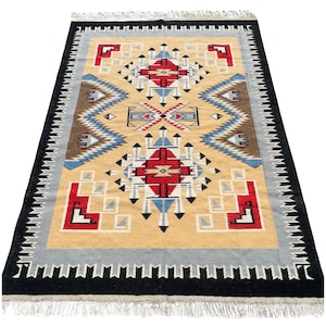 May include: Rectangular rug with a geometric pattern in beige, red, blue, and gray. The rug has a black border with a fringe on the short ends. The central design features diamond and zigzag shapes.