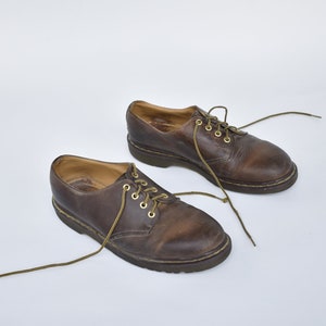 May include: A pair of brown leather lace-up shoes with gold eyelets. The shoes have a worn look and are on a white background.
