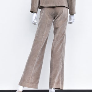 May include: A tan corduroy suit on a mannequin. The suit comprises a jacket and wide-leg trousers. The fabric has a ribbed texture. The mannequin is set against a white backdrop.
