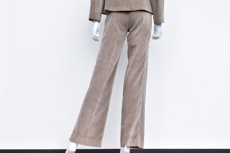 May include: A tan corduroy suit on a mannequin. The suit comprises a jacket and wide-leg trousers. The fabric has a ribbed texture. The mannequin is set against a white backdrop.