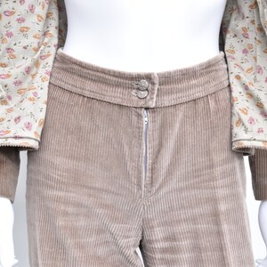 May include: A tan corduroy suit, comprising a jacket with a floral lining and trousers. The trousers feature a zip and button fastening. The suit is displayed on a mannequin.