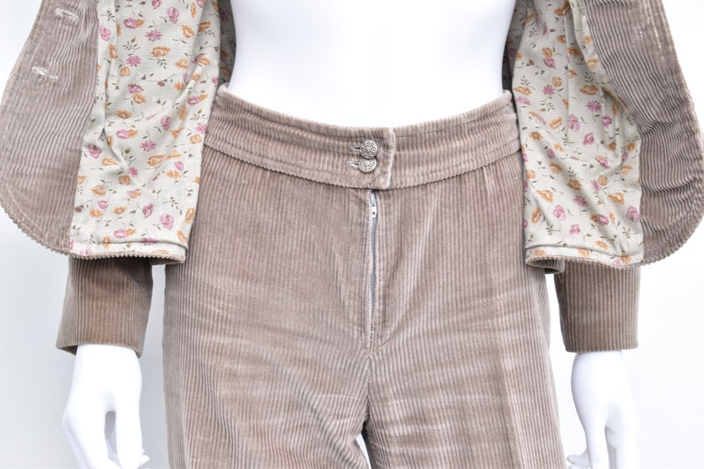 May include: A tan corduroy suit, comprising a jacket with a floral lining and trousers. The trousers feature a zip and button fastening. The suit is displayed on a mannequin.